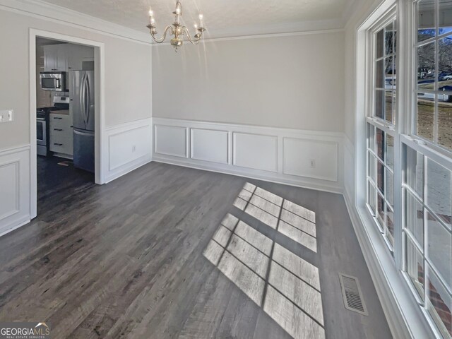 unfurnished dining area featuring visible vents, dark wood-style floors, ornamental molding, a decorative wall, and a notable chandelier