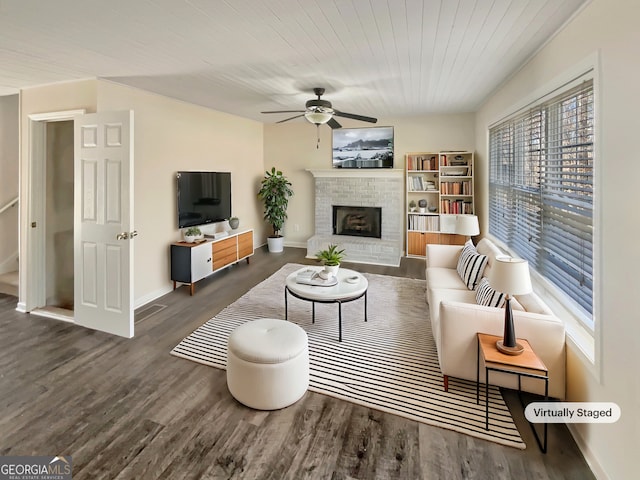 living area with a ceiling fan, a brick fireplace, baseboards, and wood finished floors