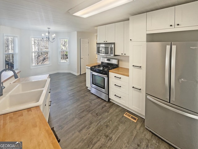 kitchen with wooden counters, appliances with stainless steel finishes, dark wood-type flooring, white cabinets, and a sink