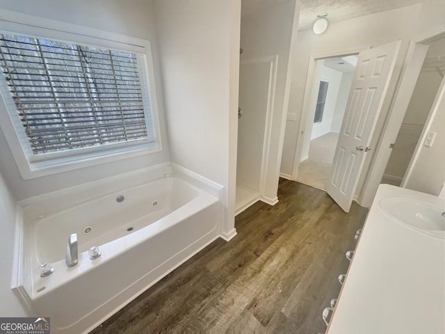 full bathroom featuring walk in shower, a sink, a jetted tub, and wood finished floors