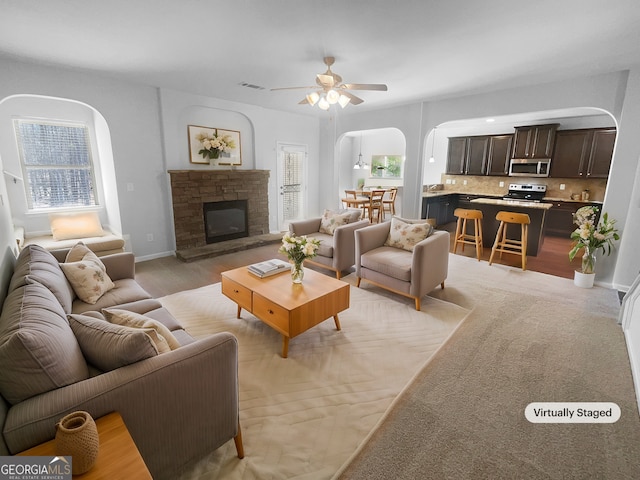 living area with visible vents, arched walkways, baseboards, ceiling fan, and a stone fireplace