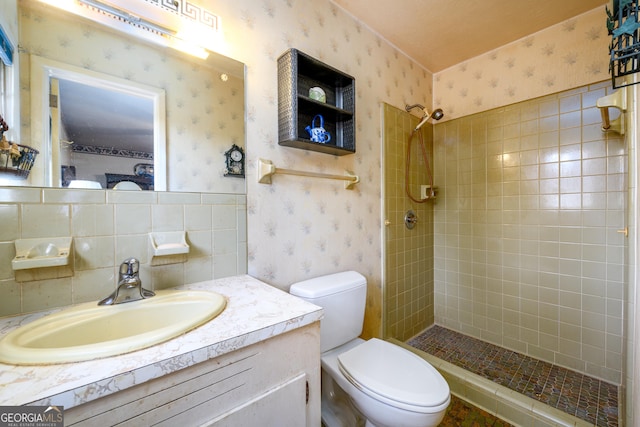 full bath with tiled shower, vanity, toilet, and wallpapered walls