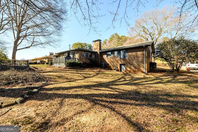 rear view of property featuring a yard, brick siding, a chimney, and cooling unit