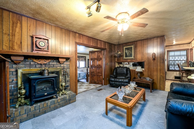 living room featuring a wood stove, wooden walls, a ceiling fan, and a textured ceiling