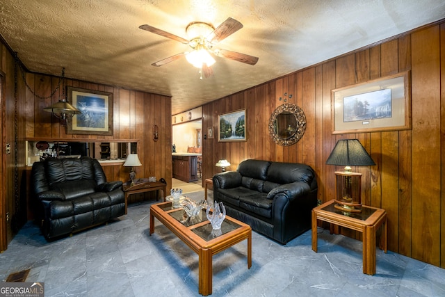 living room featuring wood walls, a textured ceiling, and ceiling fan