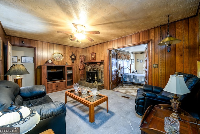 living area with visible vents, a wood stove, wood walls, a textured ceiling, and ceiling fan