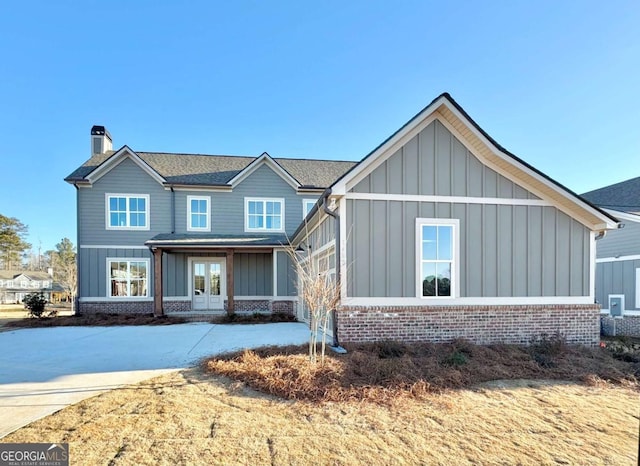 view of front facade with board and batten siding, french doors, brick siding, and a chimney