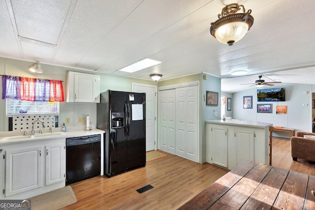 kitchen featuring light wood finished floors, light countertops, white cabinetry, a sink, and black appliances