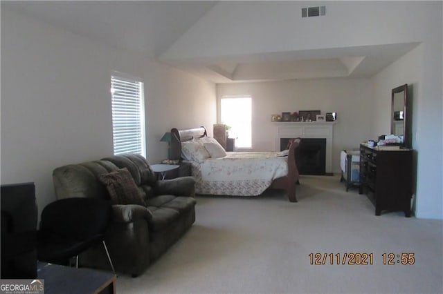 carpeted bedroom with vaulted ceiling, a raised ceiling, visible vents, and a fireplace with raised hearth