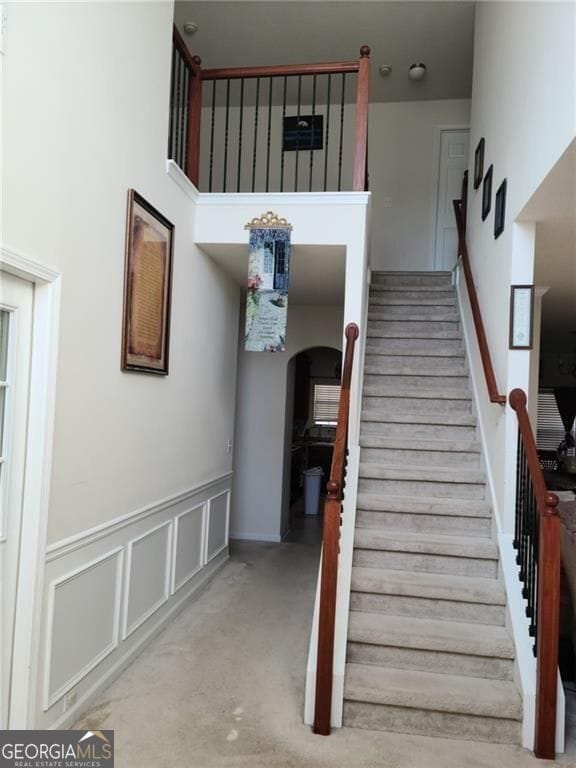 stairway featuring a towering ceiling, a wainscoted wall, arched walkways, and a decorative wall