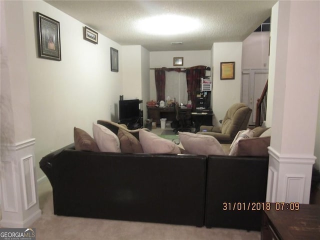 living area with a textured ceiling, carpet, and decorative columns