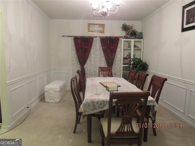 carpeted dining area with ornamental molding, a decorative wall, and an inviting chandelier