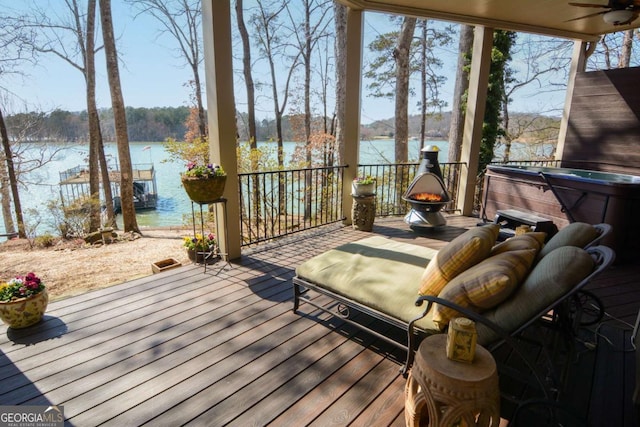 wooden deck with a water view, ceiling fan, and a hot tub