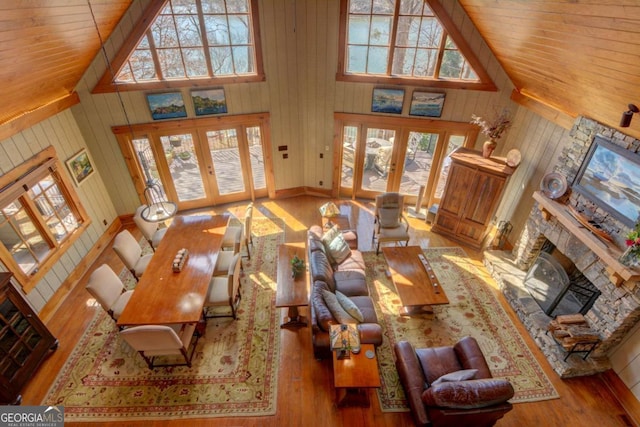 living room featuring high vaulted ceiling, french doors, wood-type flooring, and a stone fireplace