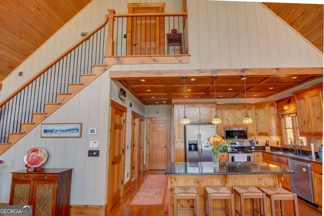 kitchen featuring light wood finished floors, dark countertops, wooden ceiling, stainless steel appliances, and a sink