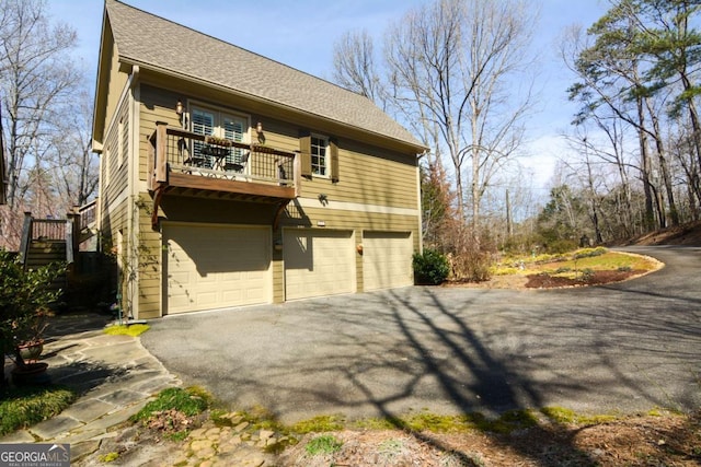 exterior space featuring driveway, roof with shingles, an attached garage, and a balcony