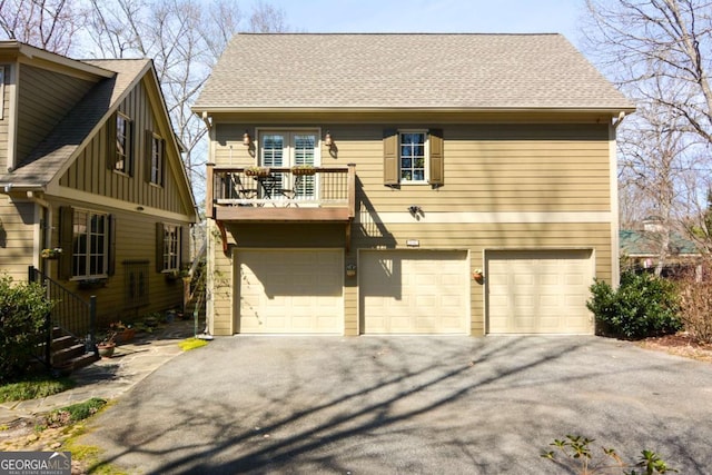 view of front facade featuring a garage, driveway, a shingled roof, and a balcony