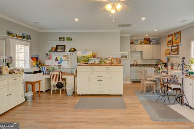 kitchen featuring a sink, visible vents, ornamental molding, light wood finished floors, and tasteful backsplash