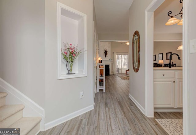 hallway with light wood finished floors, baseboards, stairway, and a sink