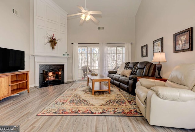 living room featuring light wood finished floors, visible vents, a ceiling fan, and a high end fireplace