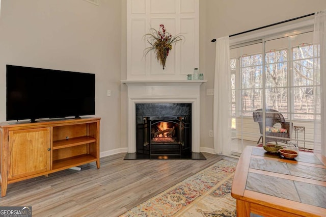 living room with a high end fireplace, light wood-style flooring, and baseboards