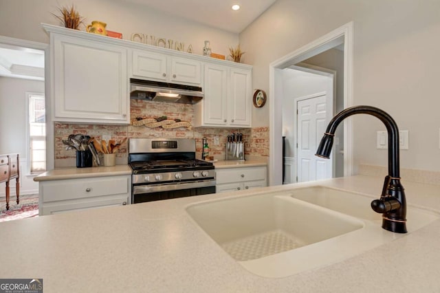 kitchen featuring under cabinet range hood, a sink, light countertops, tasteful backsplash, and gas stove