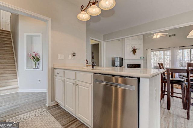 kitchen featuring light wood finished floors, ceiling fan, light countertops, white cabinetry, and stainless steel dishwasher