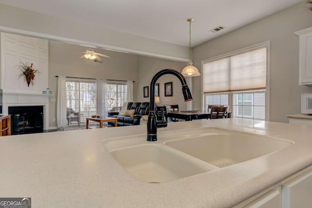 details featuring pendant lighting, a fireplace, light countertops, visible vents, and a sink