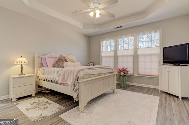 bedroom with wood finished floors, visible vents, baseboards, a tray ceiling, and crown molding