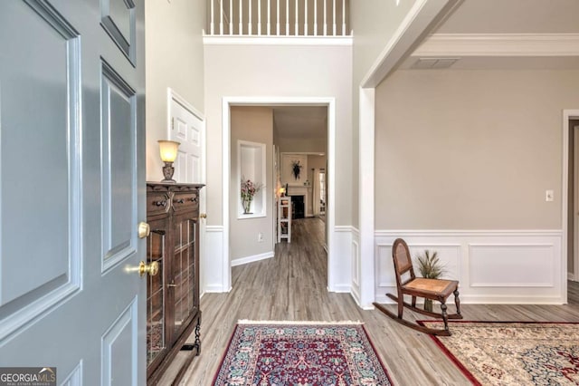 entryway featuring visible vents, a wainscoted wall, ornamental molding, wood finished floors, and a decorative wall