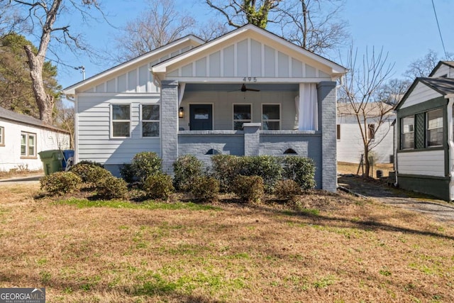 bungalow-style home with board and batten siding, a front yard, brick siding, and a ceiling fan