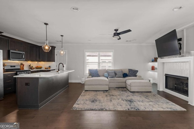 living room with a ceiling fan, ornamental molding, dark wood-type flooring, a fireplace, and recessed lighting