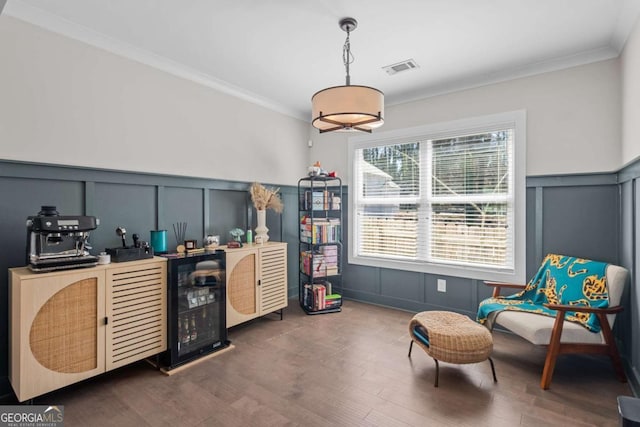 living area with visible vents, wainscoting, dark wood-style floors, crown molding, and a decorative wall