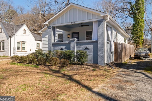 bungalow featuring ceiling fan, brick siding, fence, stone siding, and board and batten siding