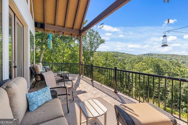 view of patio with outdoor lounge area, a view of trees, and a balcony