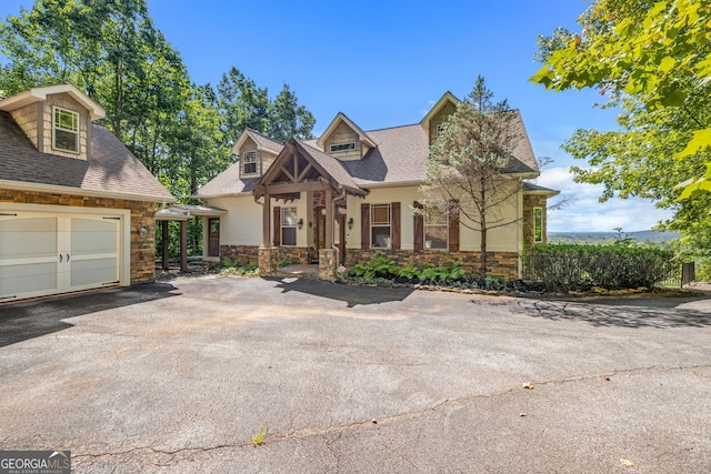 view of front facade with stone siding, roof with shingles, driveway, and stucco siding