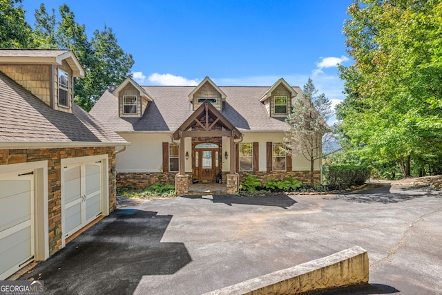 view of front of house with aphalt driveway, stone siding, roof with shingles, and a garage