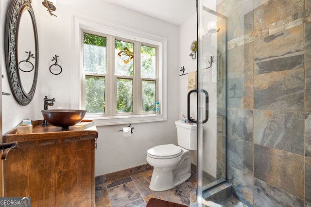 bathroom featuring toilet, vanity, baseboards, a shower stall, and stone finish floor