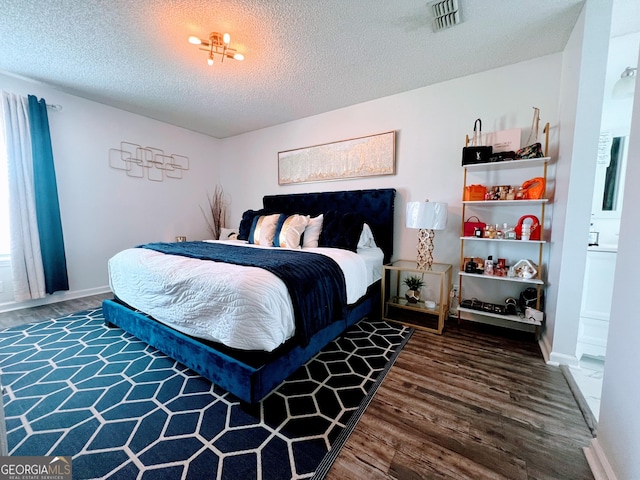 bedroom with a textured ceiling, wood finished floors, visible vents, and baseboards