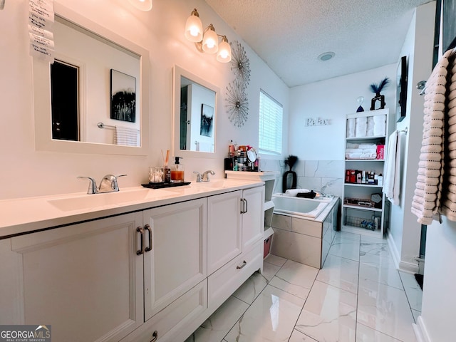 full bathroom featuring a textured ceiling, a garden tub, a sink, marble finish floor, and double vanity