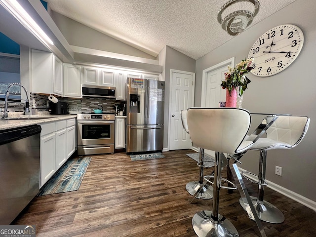 kitchen with a sink, white cabinetry, vaulted ceiling, appliances with stainless steel finishes, and dark wood finished floors