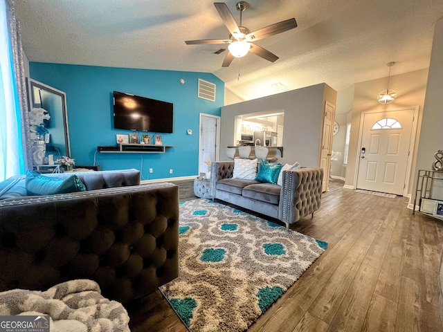 living area featuring a textured ceiling, visible vents, a ceiling fan, vaulted ceiling, and wood-type flooring