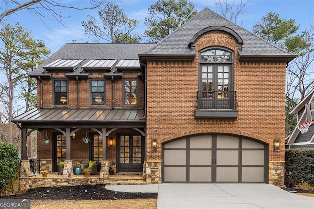 view of front facade featuring driveway, a garage, stone siding, a standing seam roof, and french doors