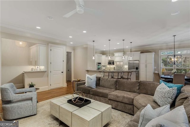 living room featuring recessed lighting, ceiling fan with notable chandelier, baseboards, ornamental molding, and light wood finished floors