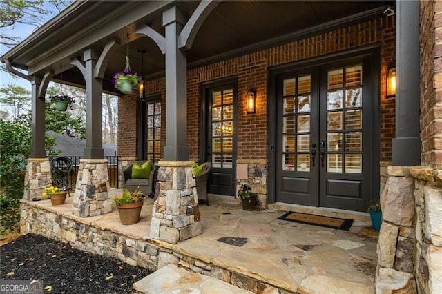 doorway to property featuring brick siding, stone siding, covered porch, and french doors