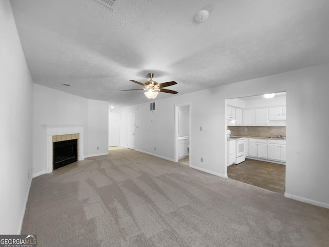 unfurnished living room with carpet floors, a tile fireplace, baseboards, and a ceiling fan