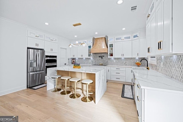 kitchen with custom exhaust hood, visible vents, appliances with stainless steel finishes, white cabinetry, and a kitchen island