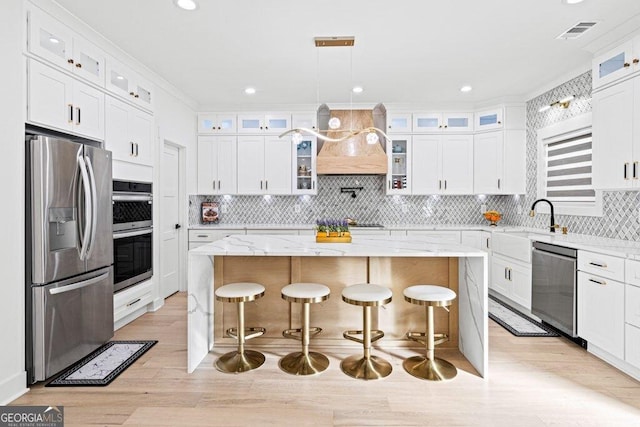 kitchen featuring a center island, custom range hood, visible vents, appliances with stainless steel finishes, and a sink