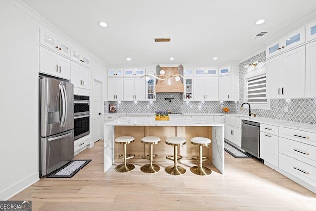 kitchen with a breakfast bar, a kitchen island, visible vents, appliances with stainless steel finishes, and custom exhaust hood