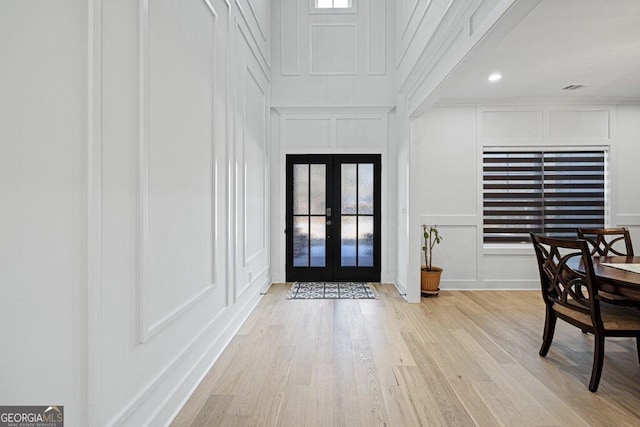 foyer featuring plenty of natural light, french doors, a decorative wall, and wood finished floors